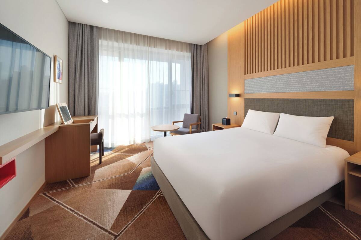 A modern hotel room with a large bed, a desk, a chair, and a TV.