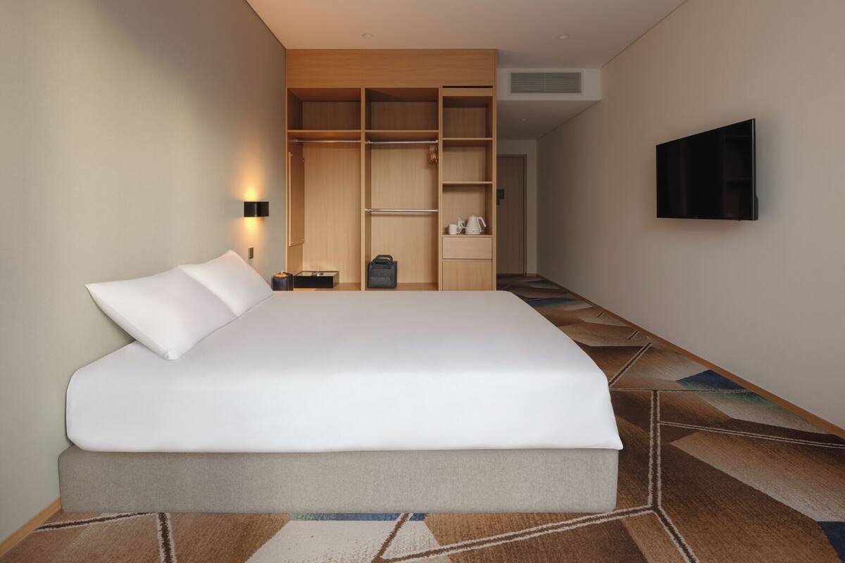 A hotel room with a large bed, a wardrobe, a television, and a small table with a kettle.
