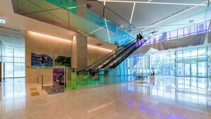 Un espacio interior amplio con piso de baldosas brillantes, barandilla de vidrio y una escalera moderna.