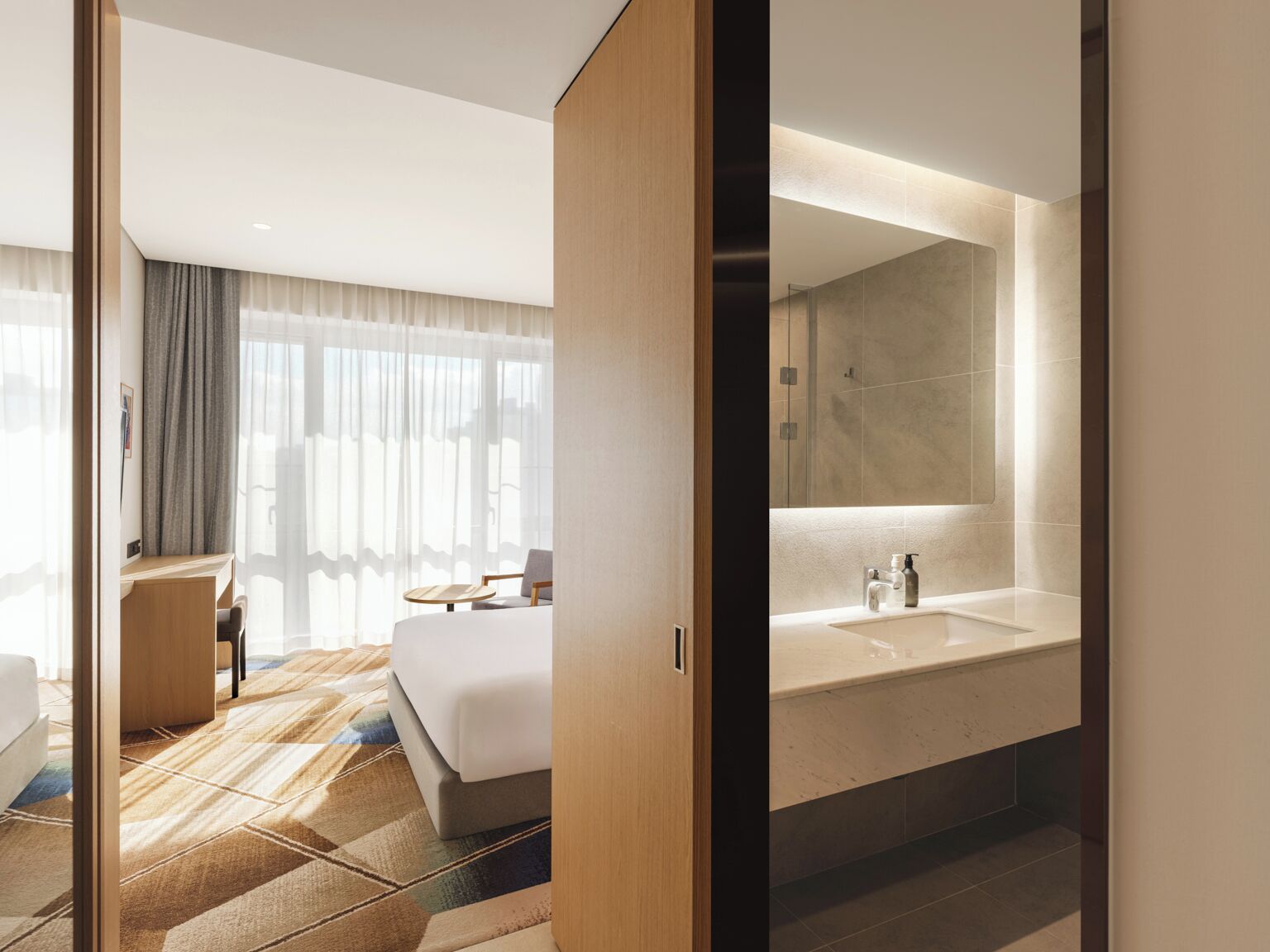 Une chambre d’hôtel moderne avec un grand lit, un bureau et une salle de bain dotée d’un grand miroir et d’un lavabo.