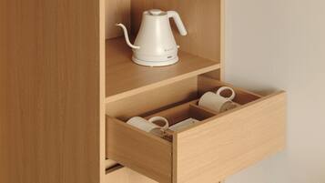 A wooden cabinet with a white kettle on top and a drawer containing two white mugs.