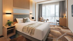 Habitación de hotel moderna con una cama grande, un escritorio, una silla y vistas a la ciudad a través de amplios ventanales.