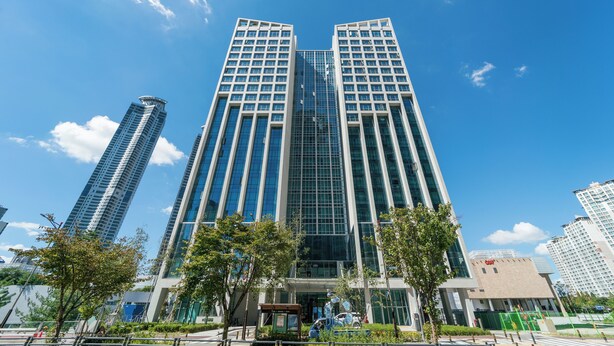 Un edificio moderno de gran altura con fachada de vidrio, rodeado de árboles y otros edificios.