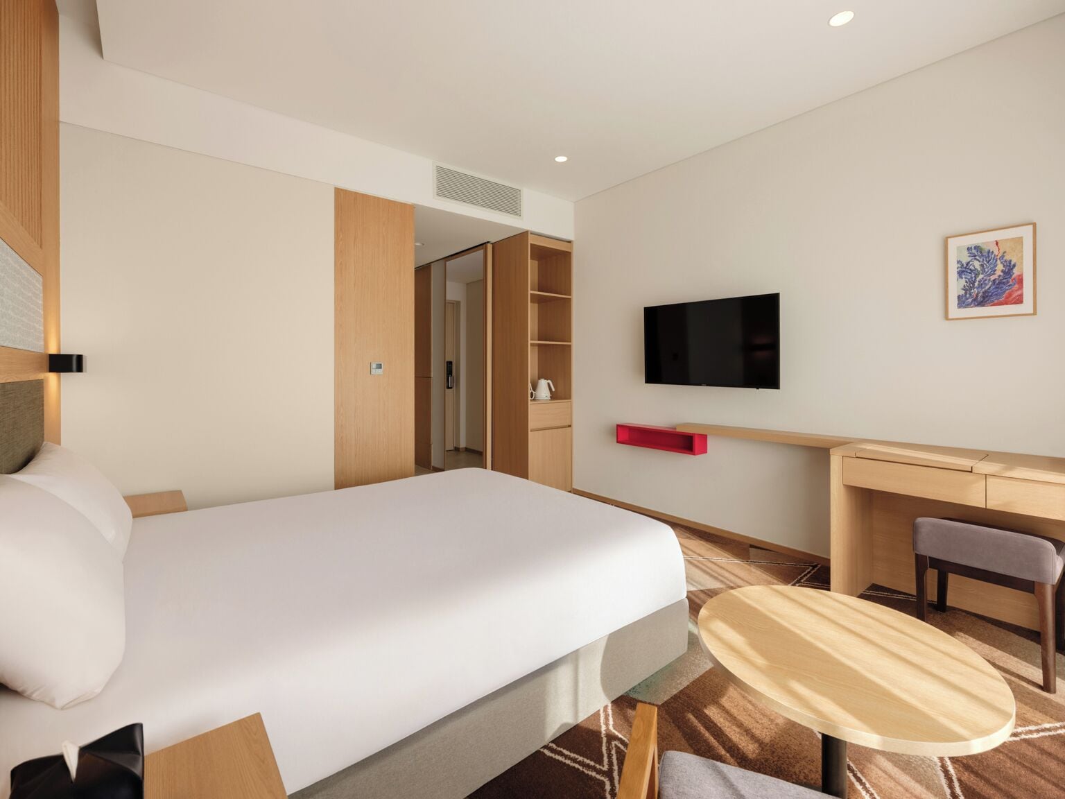 A hotel room with a bed, a desk, a chair, a TV, and a small table.