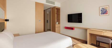 A hotel room with a bed, a desk, a chair, a TV, and a small table.