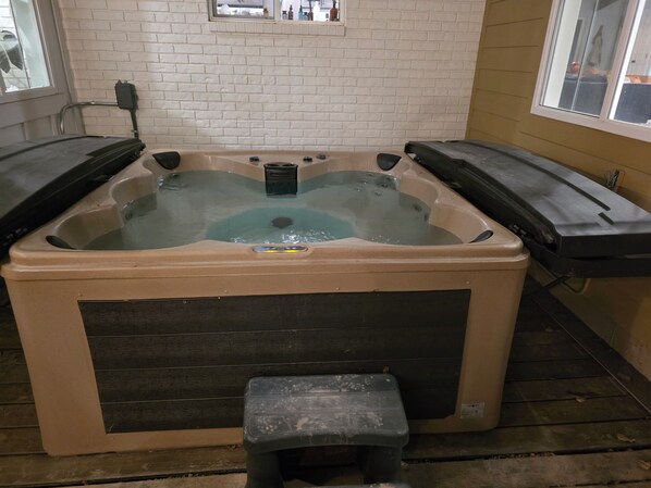 A hot tub with a control panel, a step for access, and a window in the background.