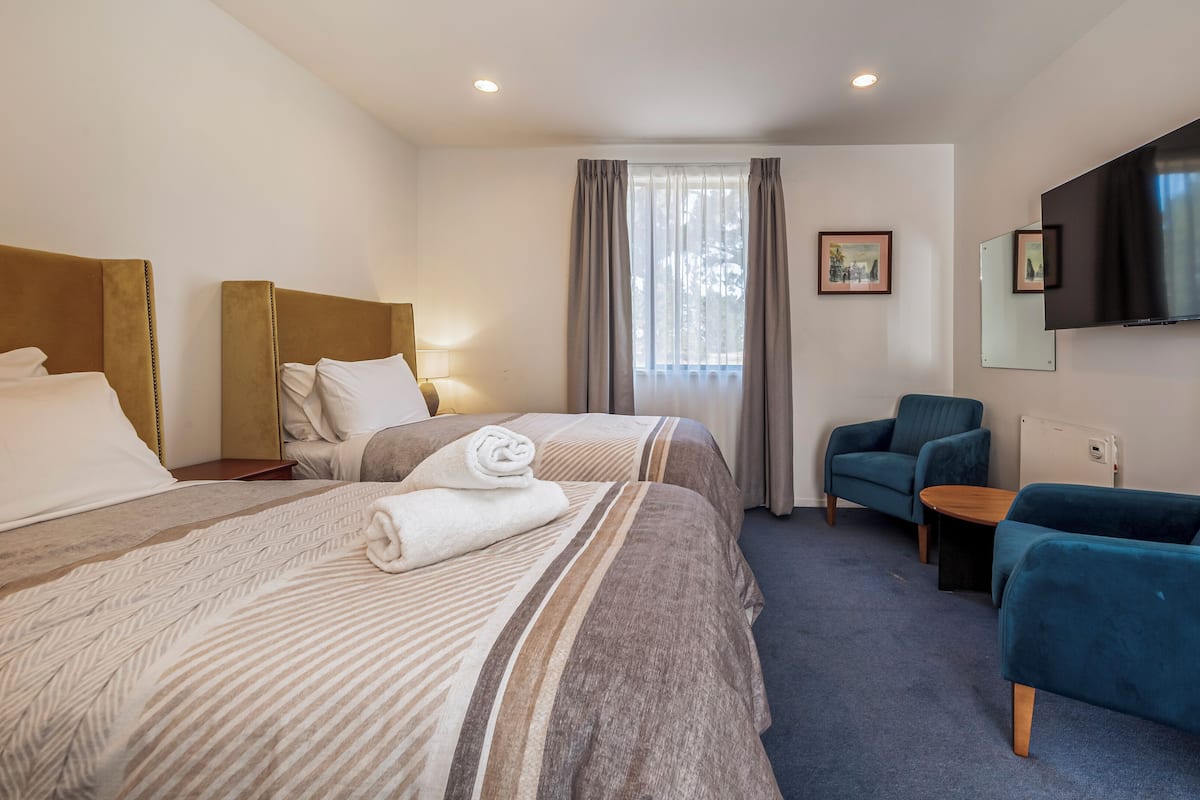 Ein Hotelzimmer mit zwei Betten, einem Fernseher, einem Sessel und einem kleinen Tisch.
