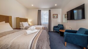 Habitación de hotel con dos camas, televisión, una silla y una mesita.