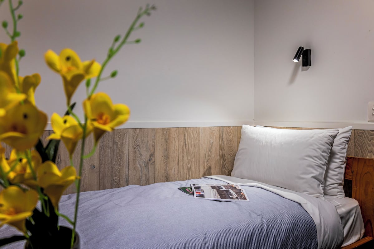 Ein ordentlich bezogenes Bett mit einer Zeitschrift, einer Wandleuchte und einem Holz-Kopfteil.