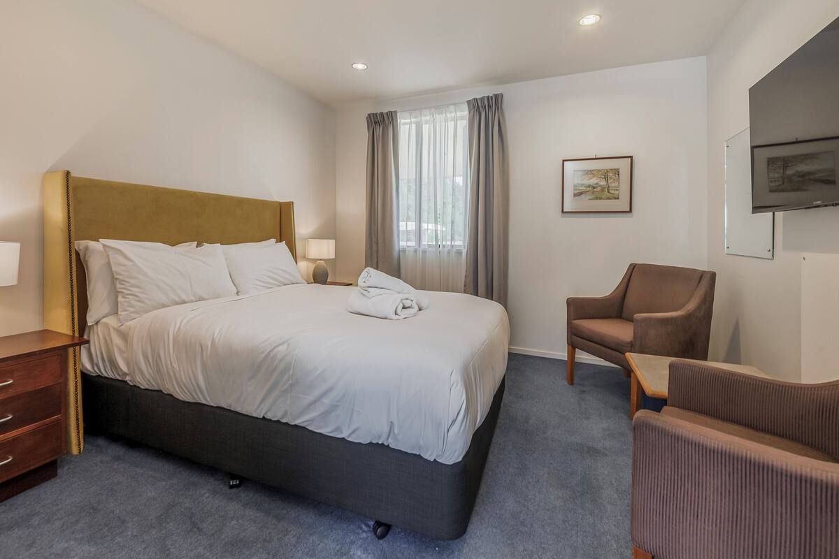 Ein Hotelzimmer mit Bett, Sessel, Schreibtisch und Fernseher.