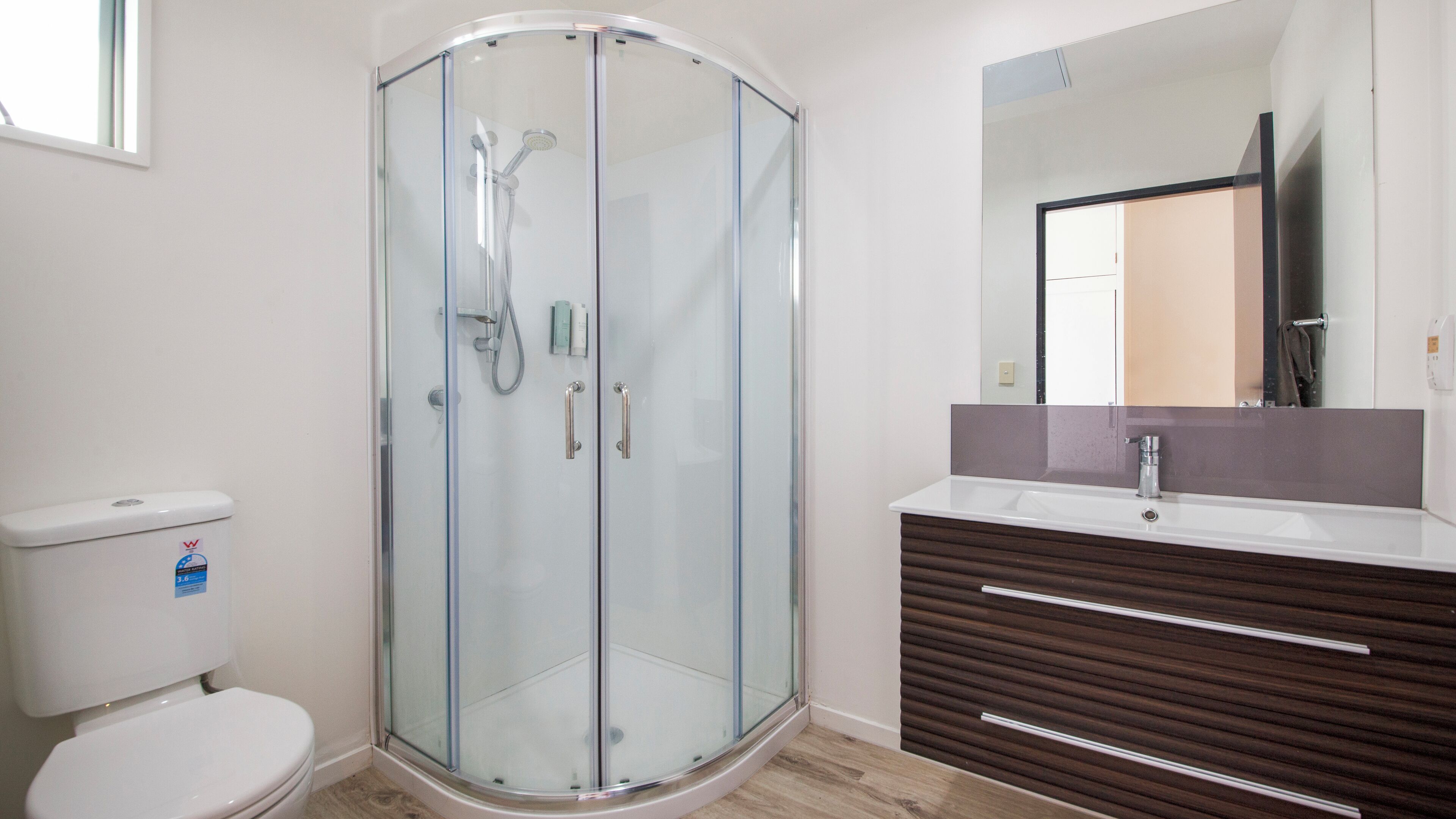 A modern bathroom with a glass-enclosed shower, a white toilet, and a wooden vanity with a mirror.