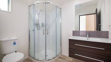 A modern bathroom with a glass-enclosed shower, a white toilet, and a wooden vanity with a mirror.