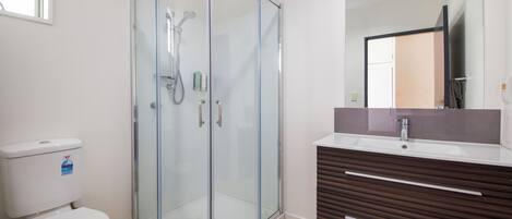 Un baño moderno con ducha de vidrio, inodoro blanco y tocador de madera con espejo.