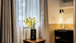 A bedroom with a wooden nightstand, a black vase with yellow flowers, a black chair, and a wooden desk with a lamp. - Harewood Lodge (Christchurch)