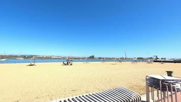A beach with a clear sky, a sandy shore, and a few boats in the water.