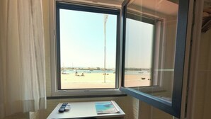 A room with a window overlooking a beach, a desk with a chair, and a remote control on the desk.