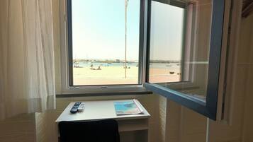 A room with a window overlooking a beach, a desk with a chair, and a remote control on the desk.