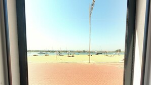 A beach view through a window with a paved walkway, boats, and a clear sky.