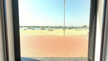 A beach view through a window with a paved walkway, boats, and a clear sky.