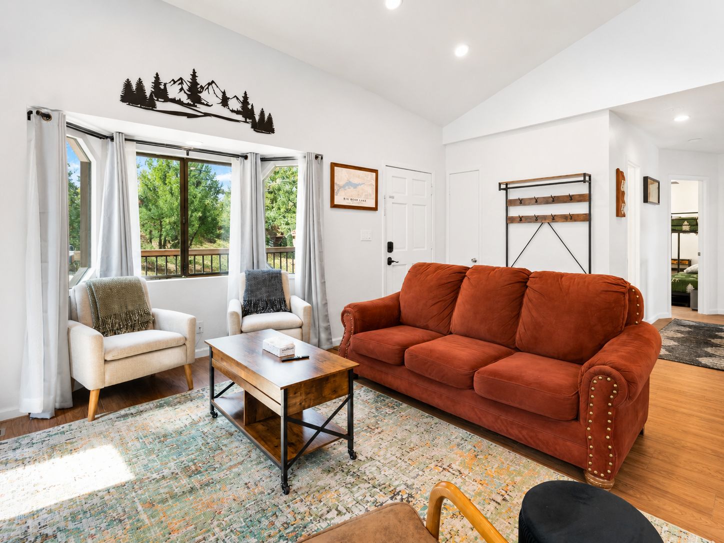 A living room with a sofa, armchairs, a coffee table, and a view of greenery outside.
