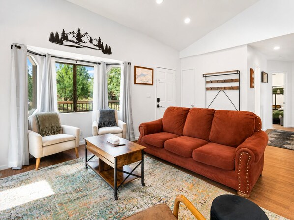Una sala de estar con un sofá, sillones, una mesa de centro y vistas al verdor exterior.