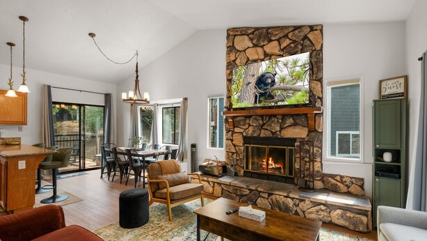 A modern living room with a stone fireplace, a dining area, and a kitchen with a wooden island.