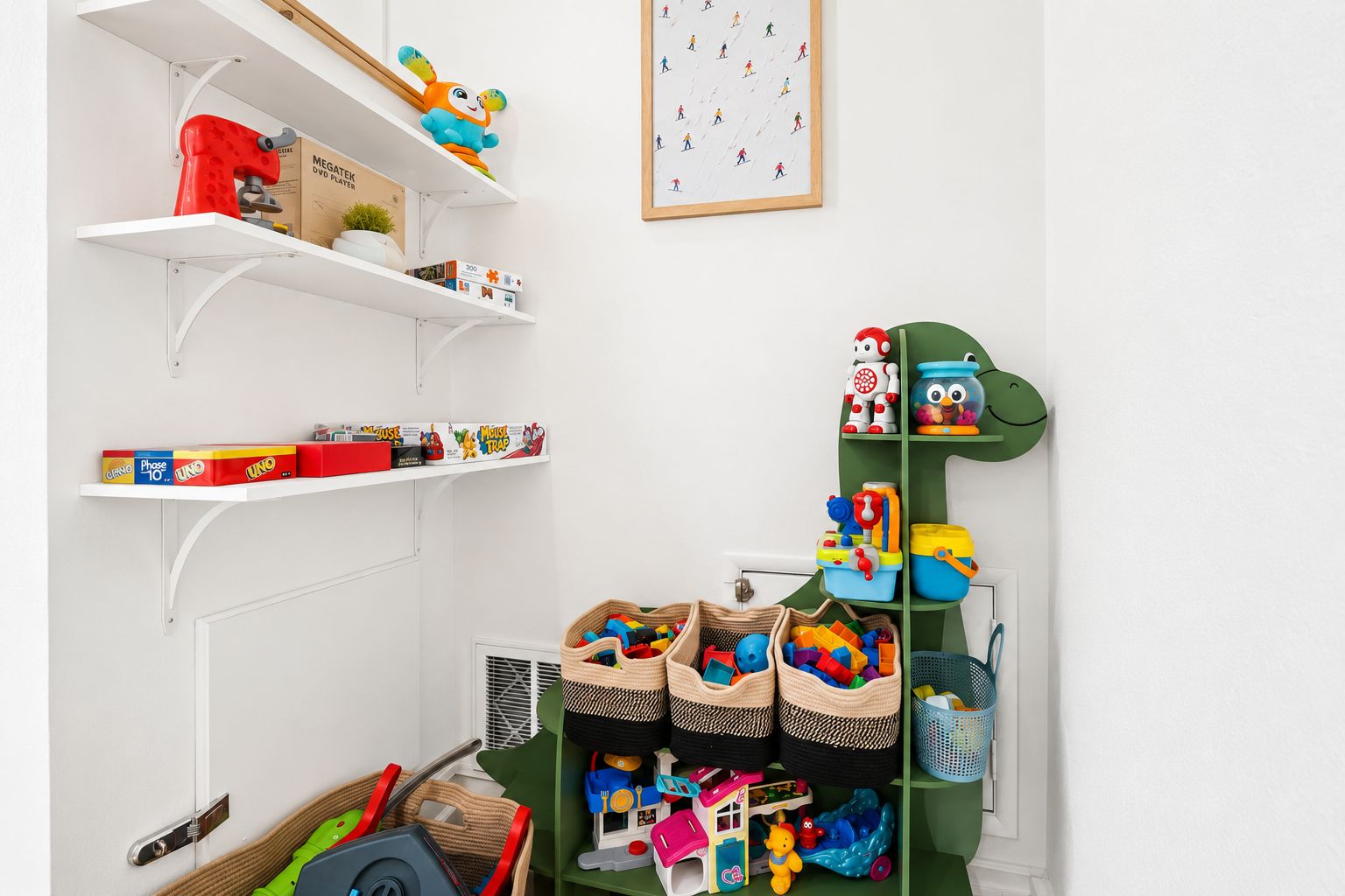 A room with white walls, a framed picture, and shelves with toys and games.