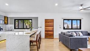 A modern kitchen with a central island, a dining area with chairs, a grey sofa, and a ceiling fan. - Quiet and elegant place in Cabo (Cabo San Lucas)