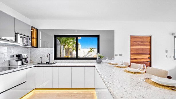 A modern kitchen with a large window, white cabinetry, and a dining area with a view. - Quiet and elegant place in Cabo (Cabo San Lucas)