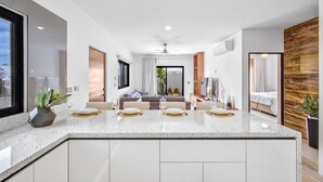 A modern kitchen with a central island, white cabinetry, and a dining area with a sofa and table set for four. - Quiet and elegant place in Cabo (Cabo San Lucas)