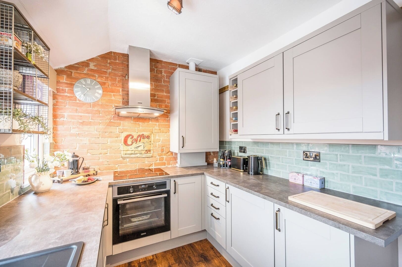 A kitchen with white cabinets, a brick wall, a coffee-themed sign, and a built-in oven.