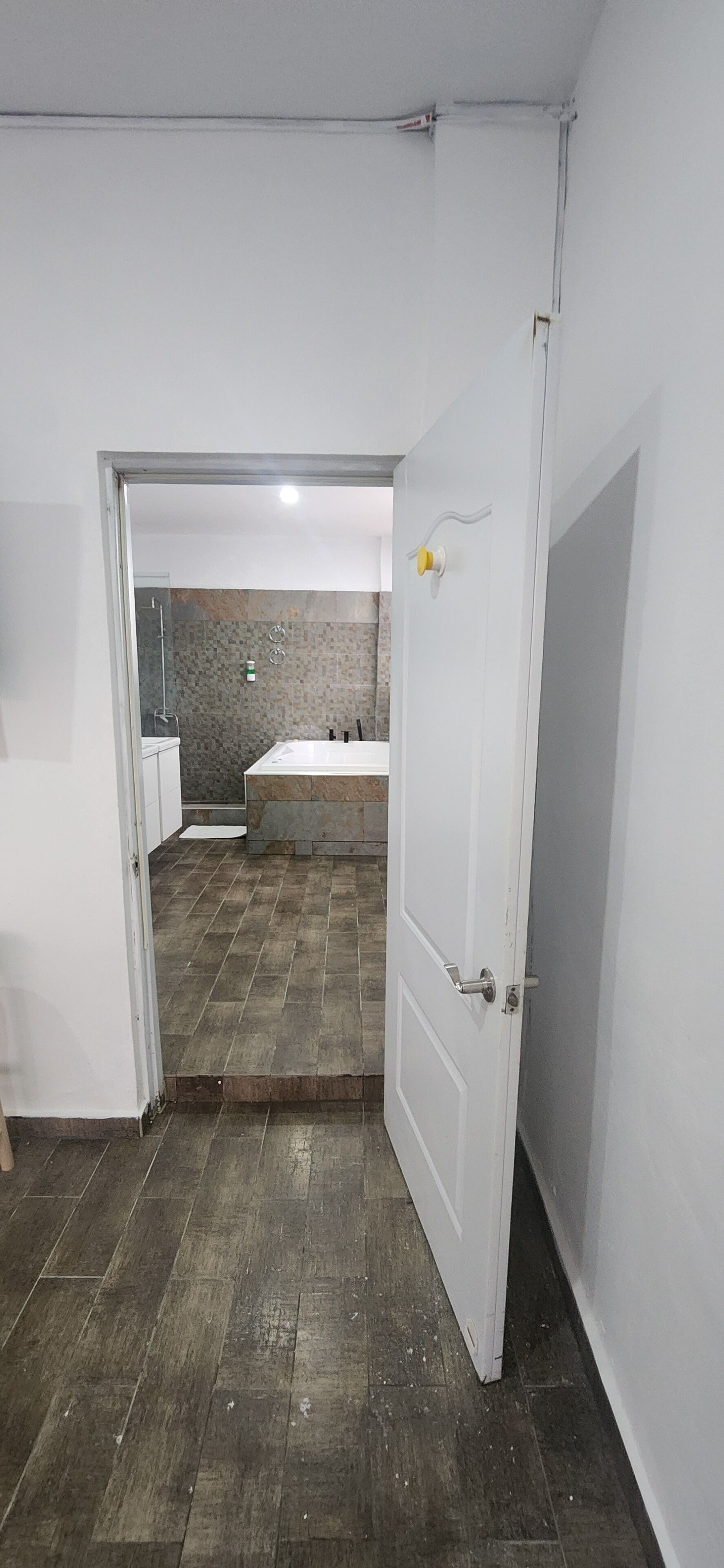 An open door leading to a bathroom with a shower, a sink, and a tiled floor.