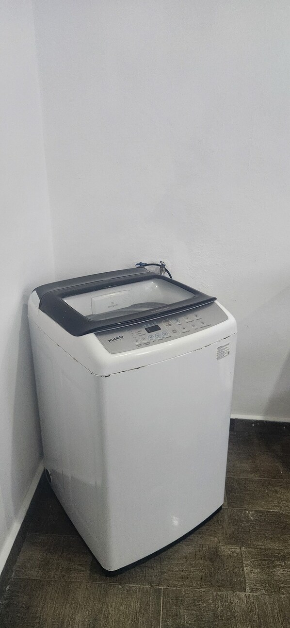 A white washing machine in a corner with a control panel and a small shelf on top.