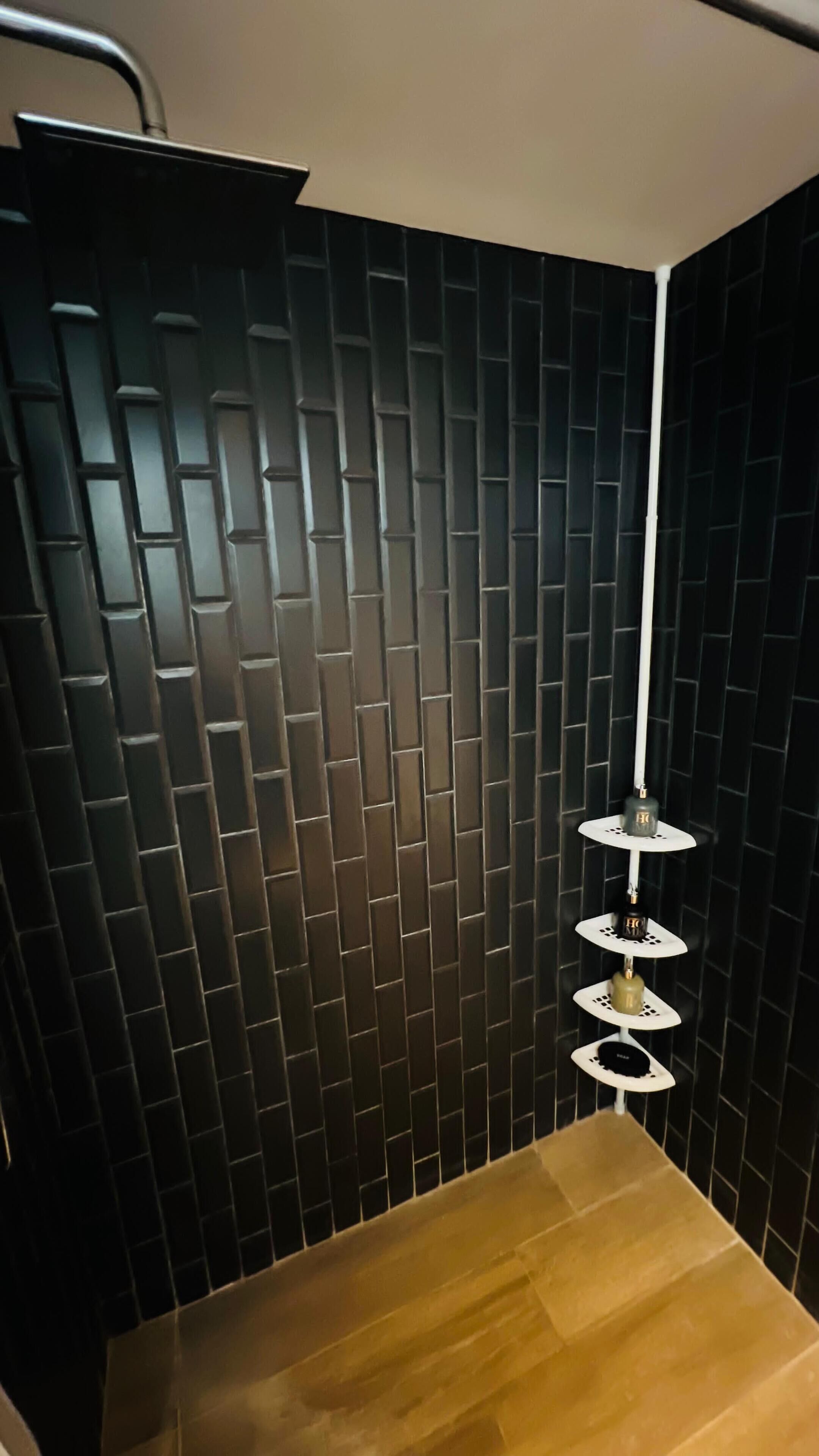 A corner of a room with a black tiled wall and a wooden floor.
