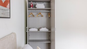 Um guarda-roupa com várias prateleiras, algumas com toalhas dobradas e cabides, e um ferro de passar na prateleira superior.