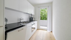 Cozinha moderna com armários brancos, bancada preta e forno embutido. Há uma janela com vista para o verde lá fora.