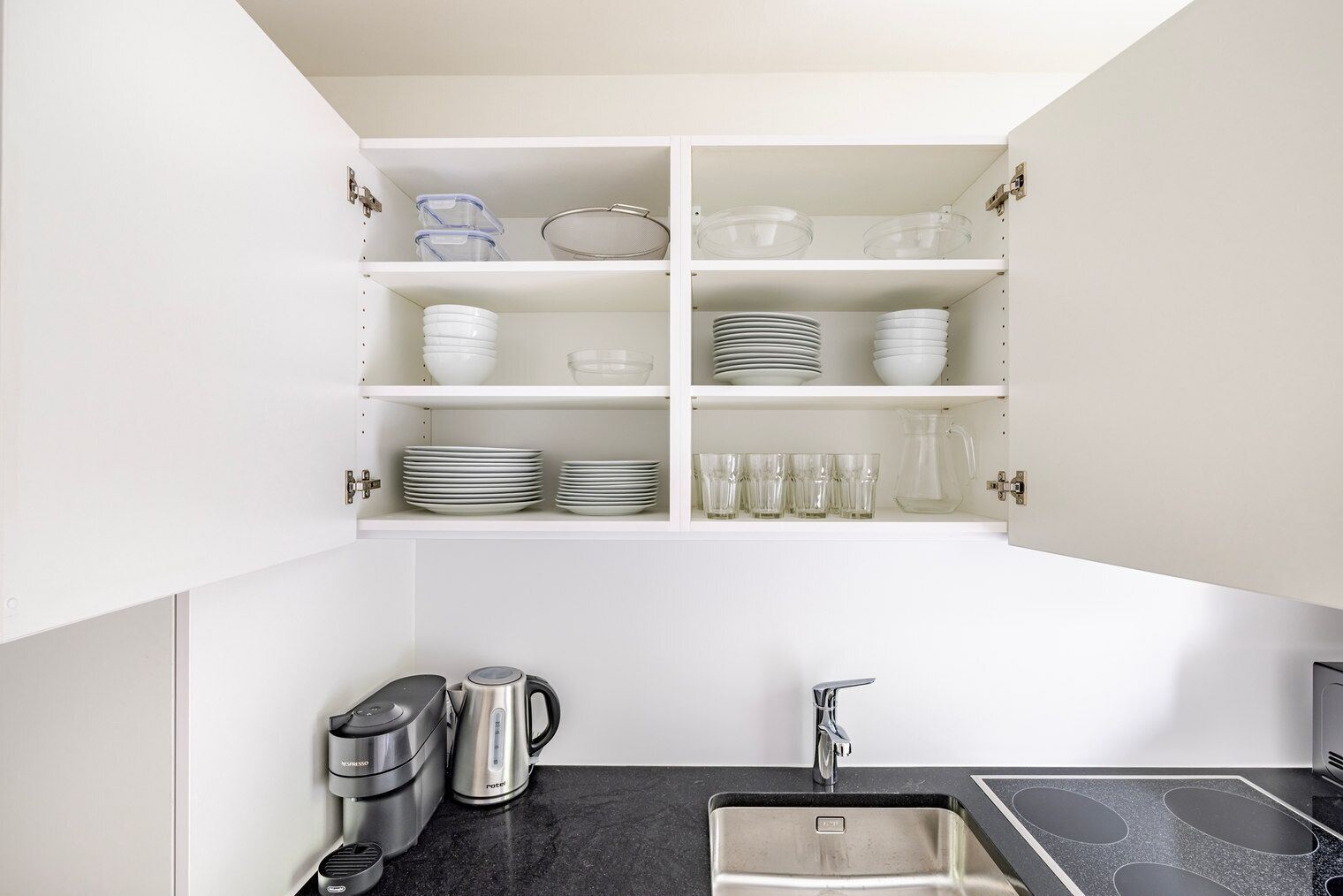 A kitchen with white cabinets, a black countertop, a stainless steel sink, and a coffee maker.