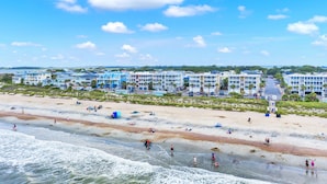 A beachfront hotel with multiple buildings, a sandy beach, and a clear sky. - Your Tybee Island Getaway! | Heated Pool Access (Tybee Island)