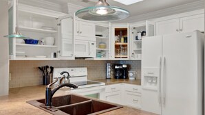 A modern kitchen with white cabinetry, a double sink, a stove, and a refrigerator. - Your Tybee Island Getaway! | Heated Pool Access (Tybee Island)
