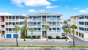 A multi-story hotel with balconies, a parking lot, and palm trees. - Your Tybee Island Getaway! | Heated Pool Access (Tybee Island)