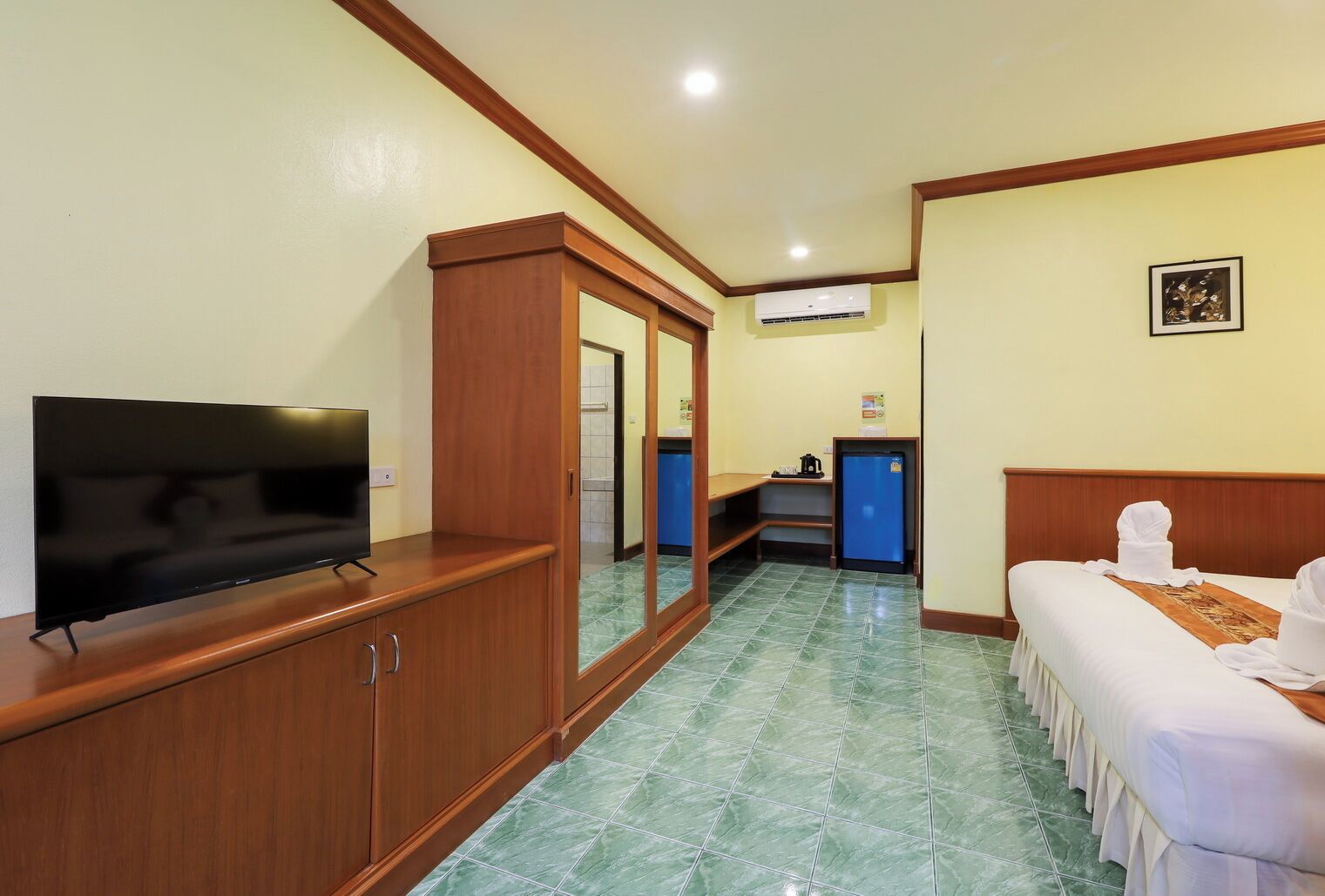 Ein Hotelzimmer mit Fernseher, Minibar, Bett und einem durch eine Tür einsehbaren Badezimmer.