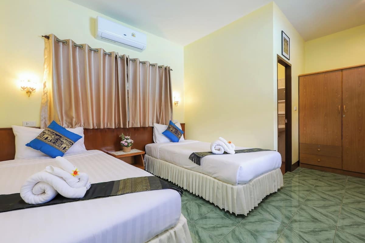 A hotel room with two beds, a wooden wardrobe, and an air conditioning unit.