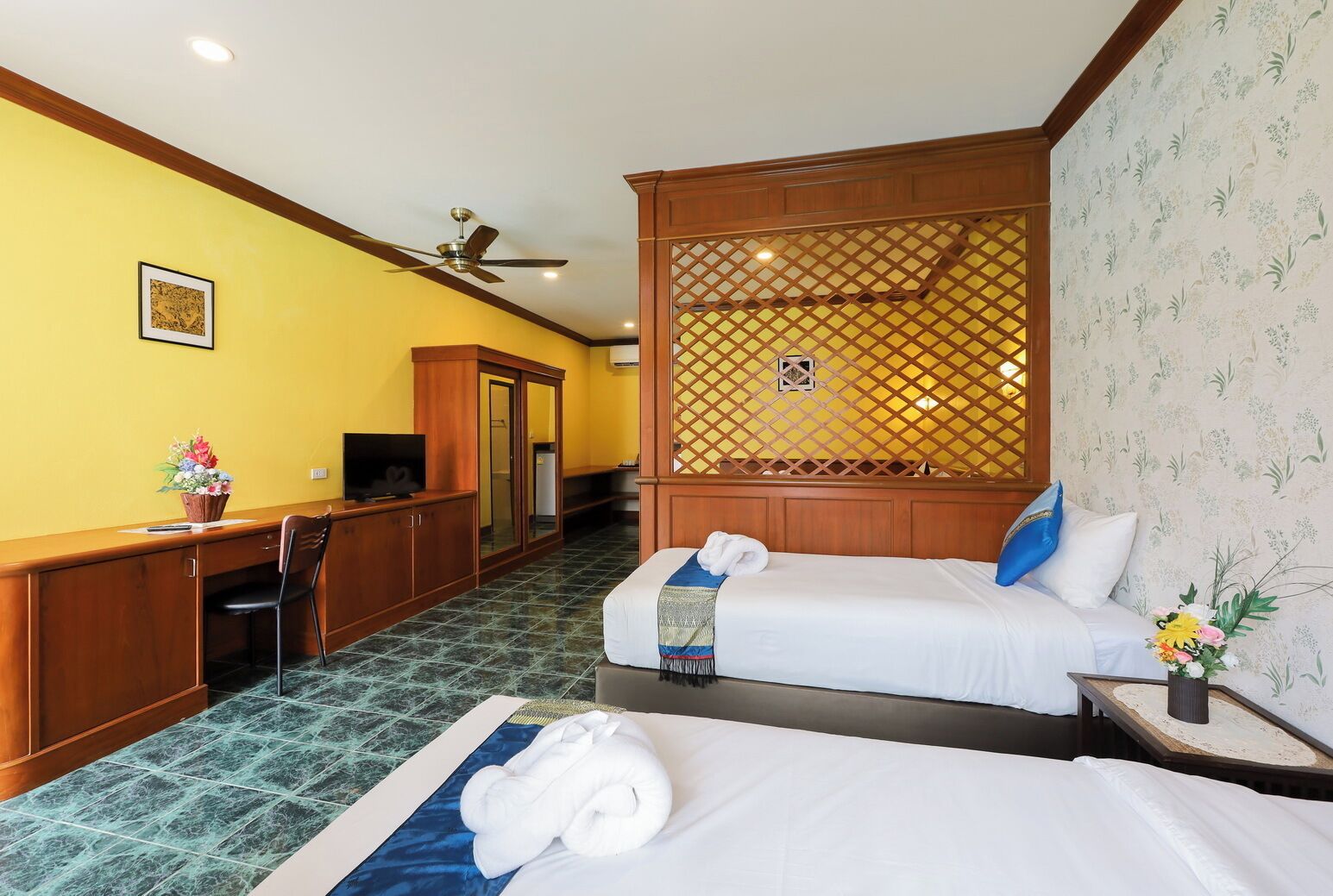 A hotel room with two beds, a desk with a chair, a TV, and a decorative partition.