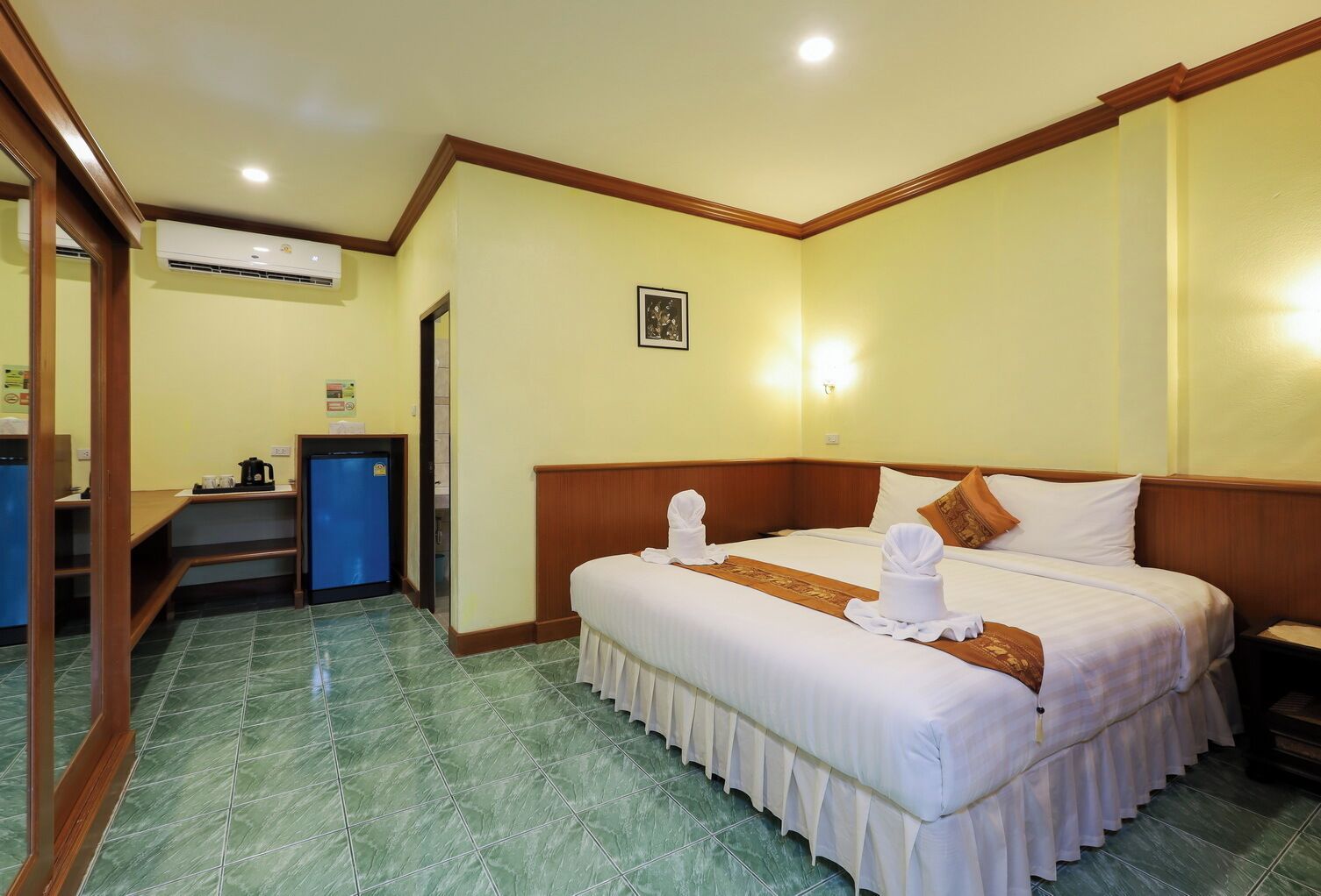 A hotel room with a bed, a desk, a coffee machine, and an air conditioning unit.
