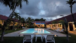A pool area with lounge chairs and palm trees, surrounded by buildings with red roofs. - The Gold-Digger's Resort (Sa Khu)