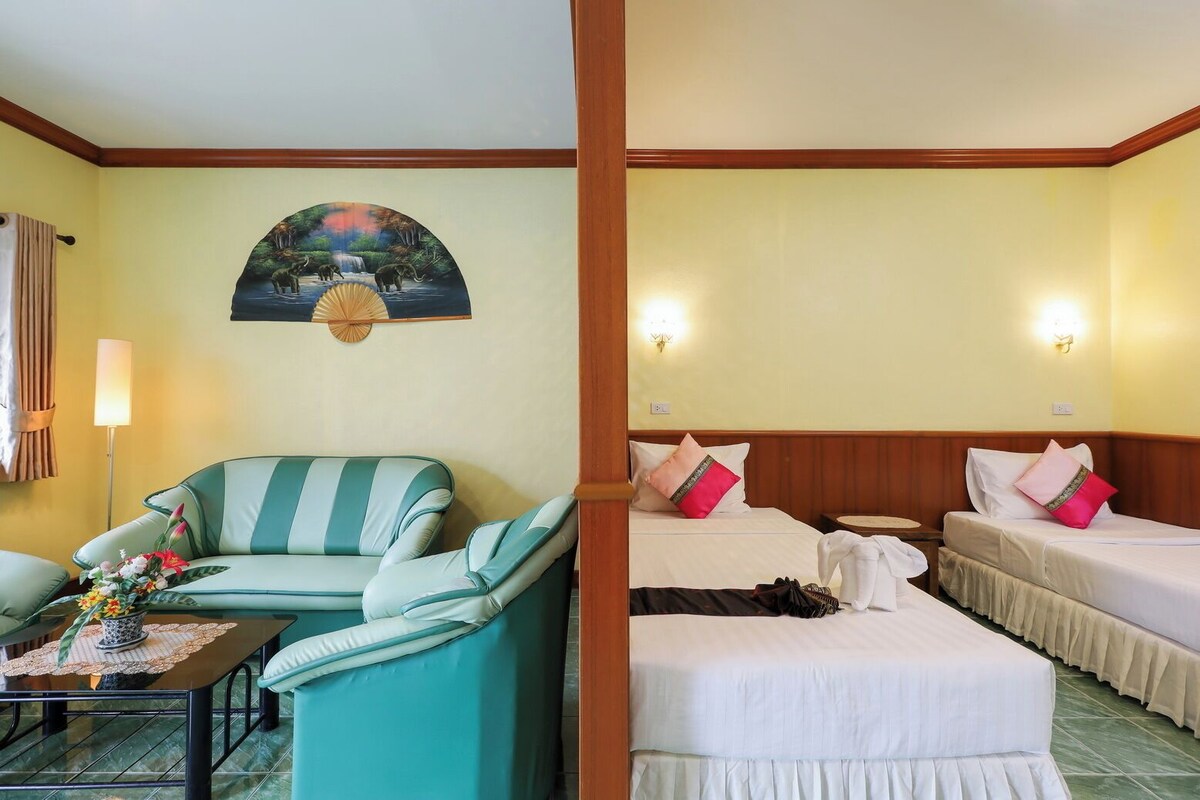 Une chambre d’hôtel avec un canapé, deux lits, un tableau accroché au mur et une petite table sur laquelle est posé un vase de fleurs.