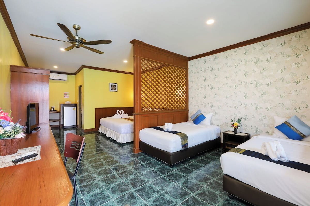 A hotel room with two beds, a desk, a chair, a ceiling fan, and a decorative screen.