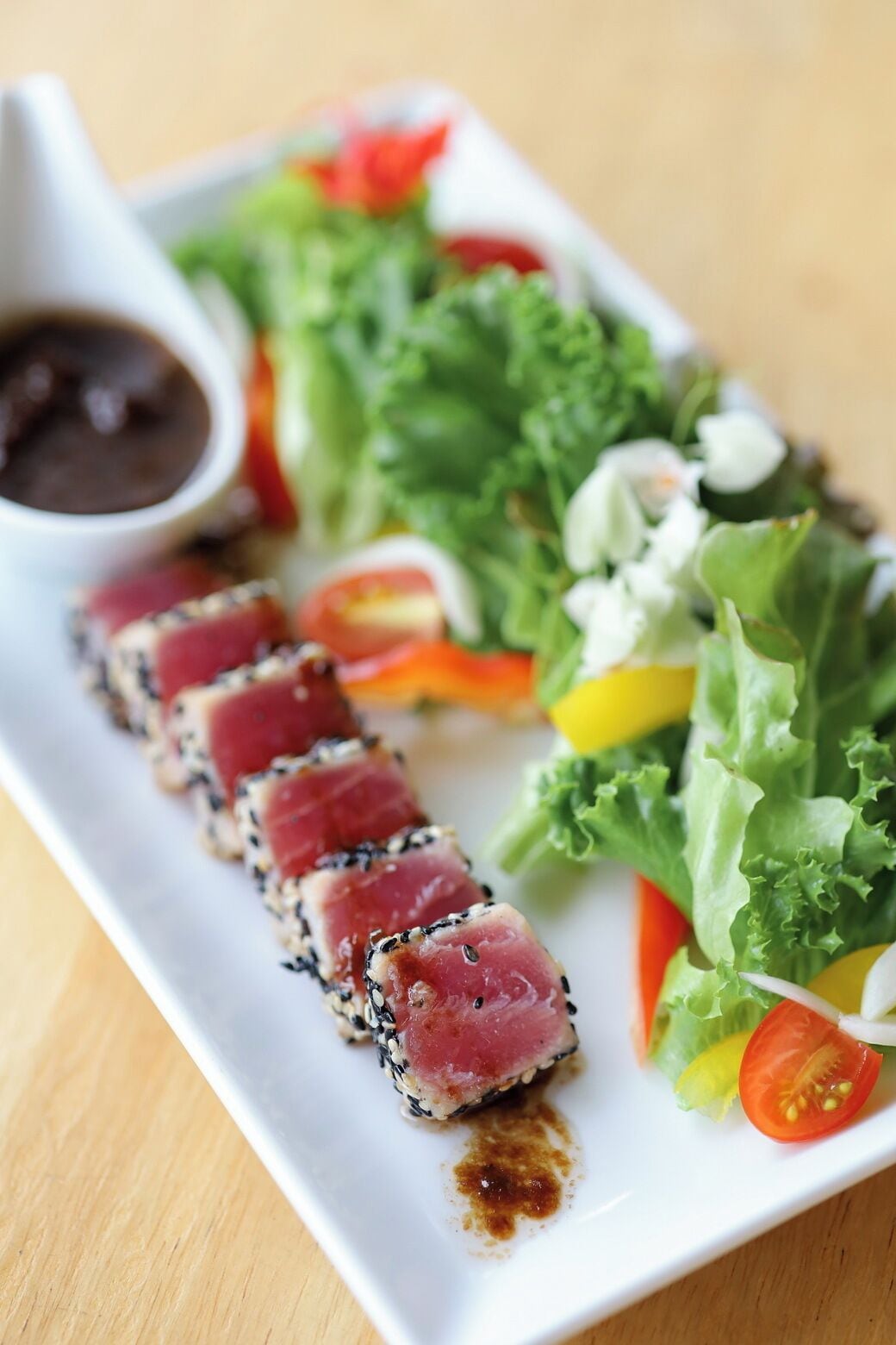 Un plato de sashimi con una guarnición de hojas verdes mezcladas y un pequeño recipiente con salsa.