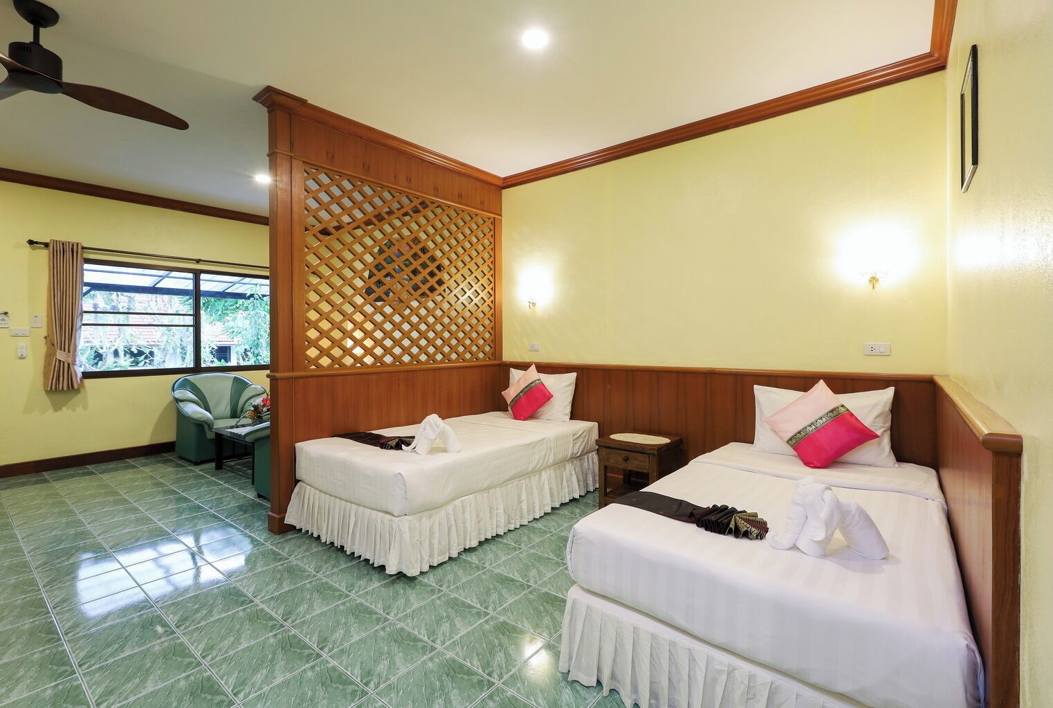 A hotel room with two single beds, a wooden headboard, a small table, a chair, and a window with curtains.