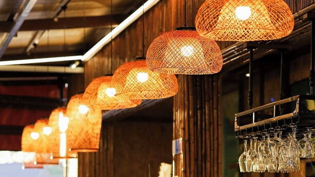 A bar area with wicker pendant lights, a counter with a glass display case, and a row of bar stools. - The Gold-Digger's Resort (Sa Khu)